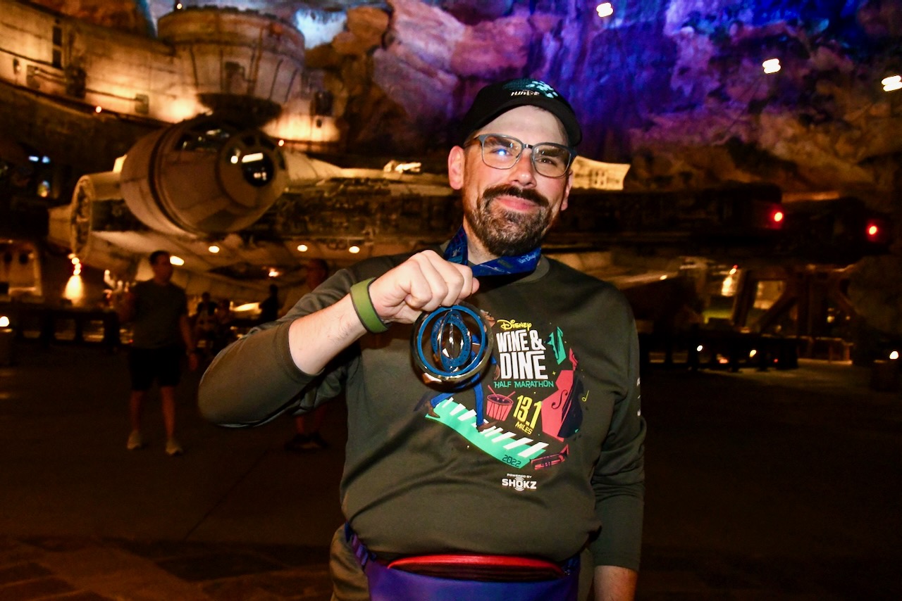 Will posing in front of the Millennium Falcon in Star Wars Galaxy's Edge at Disney's Hollywood Studios with his finisher's medal from the Wine & Dine Half Marathon in 2022.